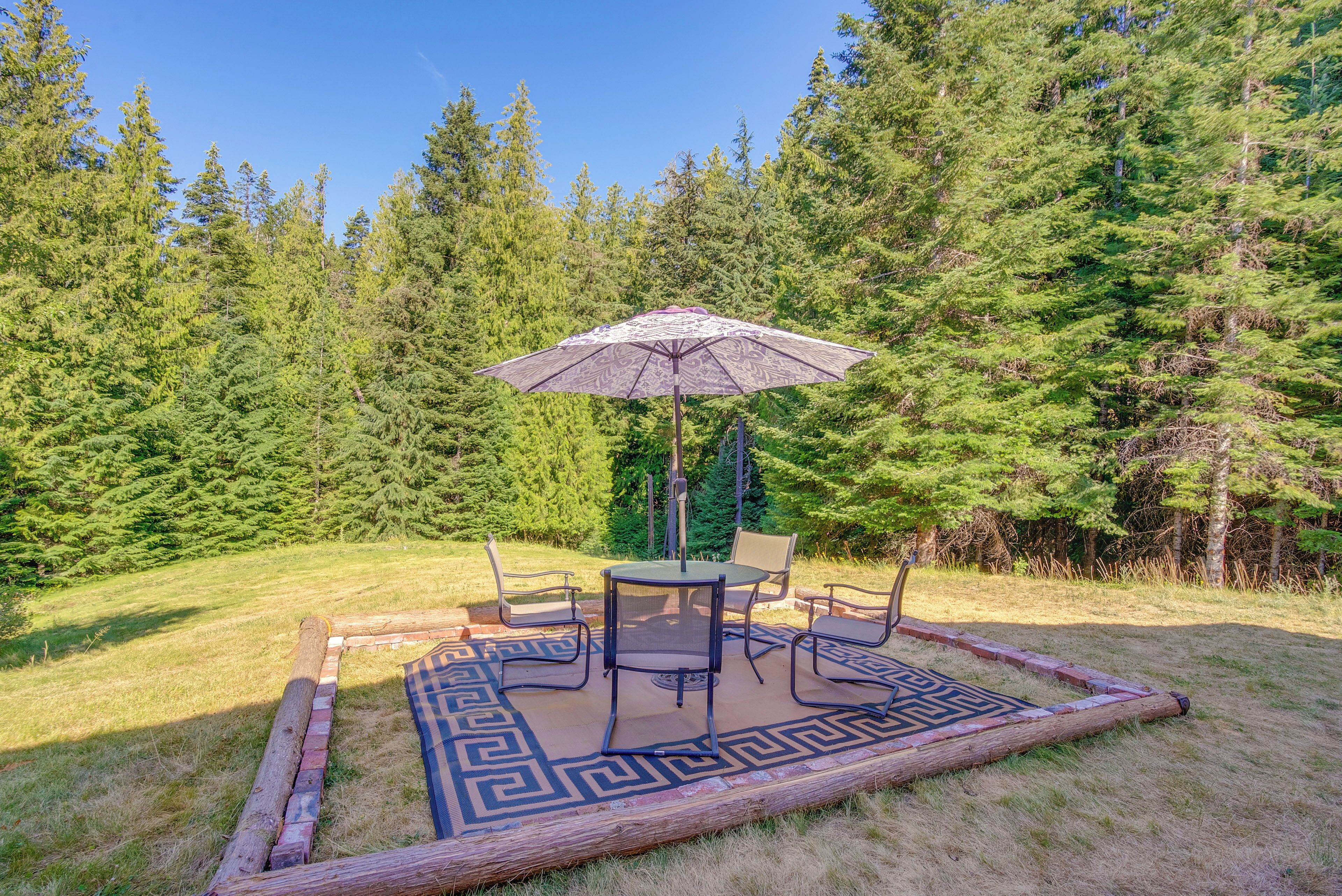 An outdoor patio with a table and chairs, surrounded by a decorative rug and a wooden fence.