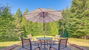 A round table with four chairs and a large umbrella in a forested outdoor area. - 11 Acres of Adventure! Woodsy Mead Stay w/ Trails (Mead)