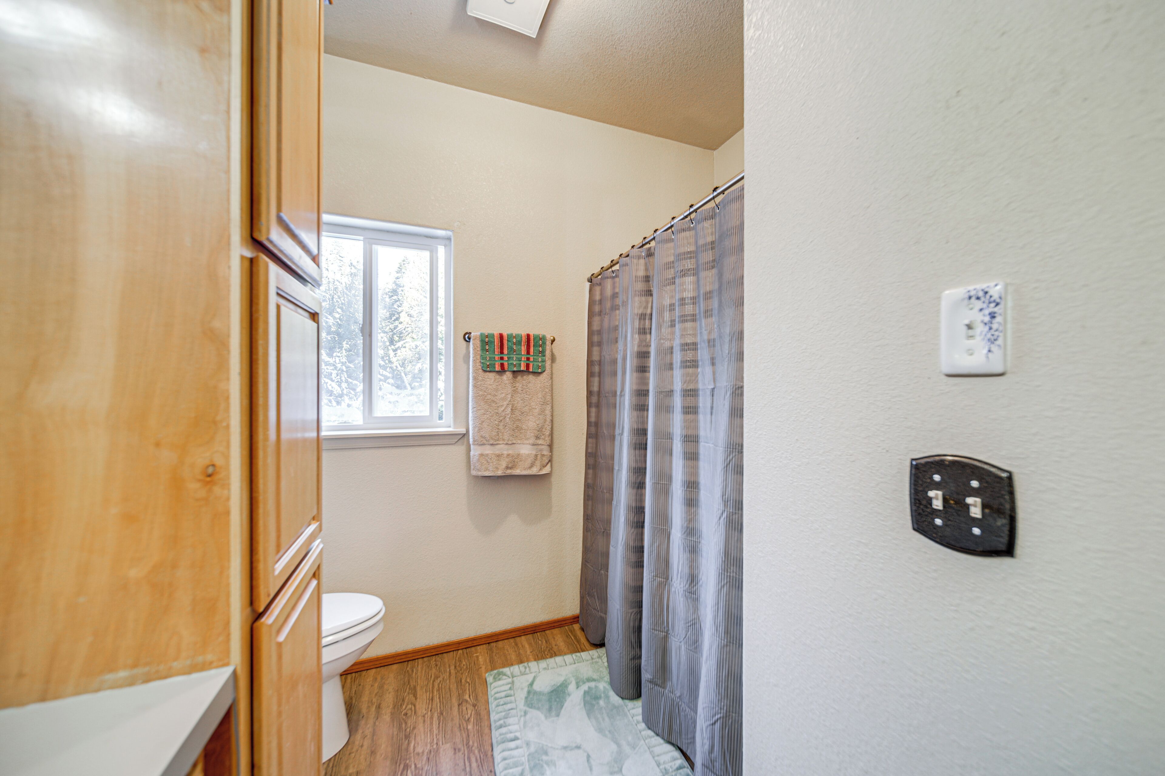 A bathroom with a toilet, a window, a towel hanging on the wall, and a shower curtain.