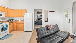 A modern kitchen with wooden cabinets, a white refrigerator, and a stove. There is a black leather sofa in the living area. - Kenai River Views & Access: Soldotna Apartment! (Soldotna)