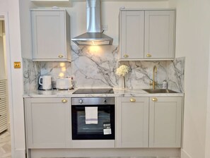 Una cucina con piani di lavoro in marmo, una cappa aspirante in acciaio inossidabile, forno a incasso e maniglie dorate.