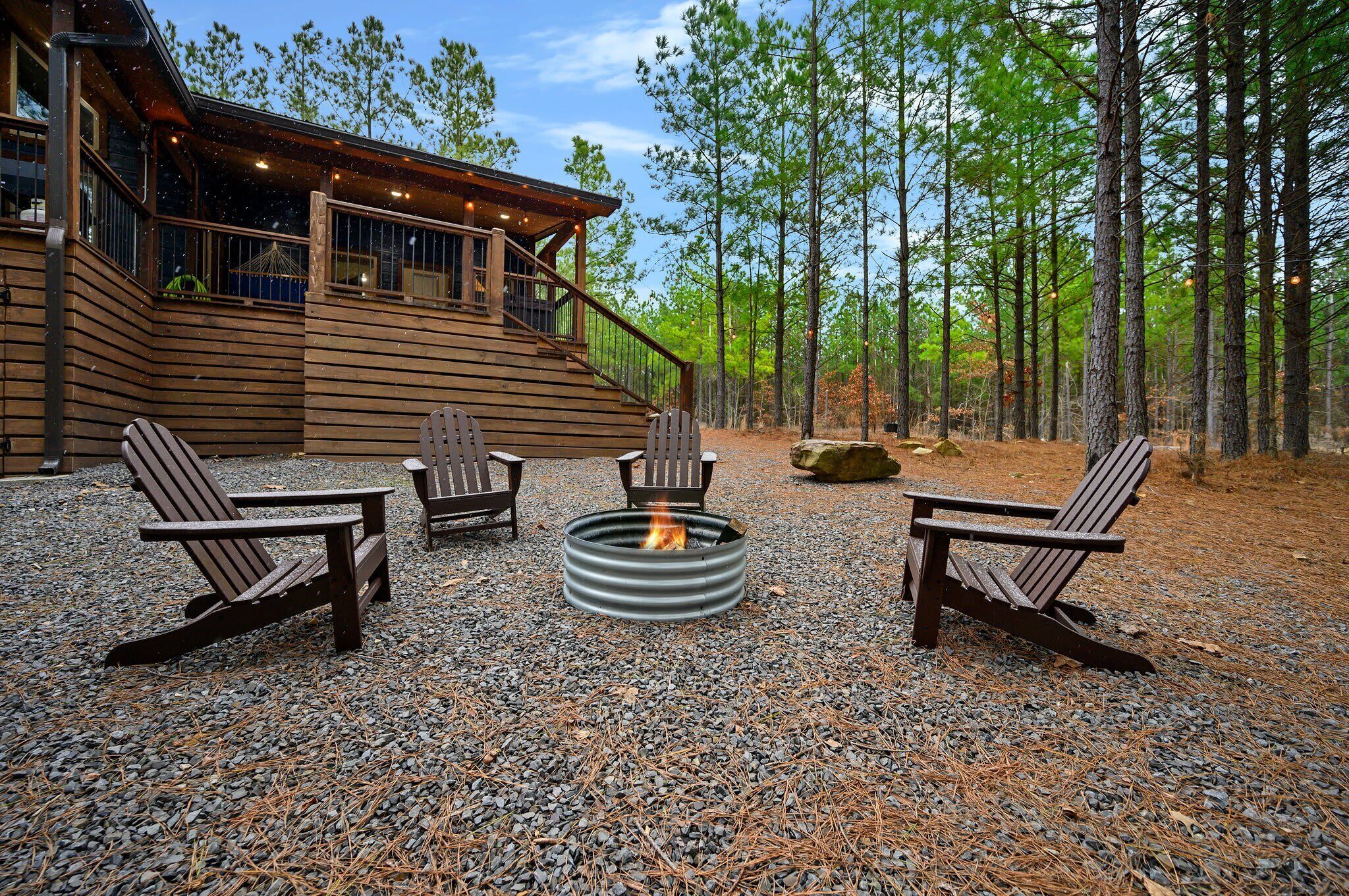 A cabin with a fire pit and Adirondack chairs in a forest setting.
