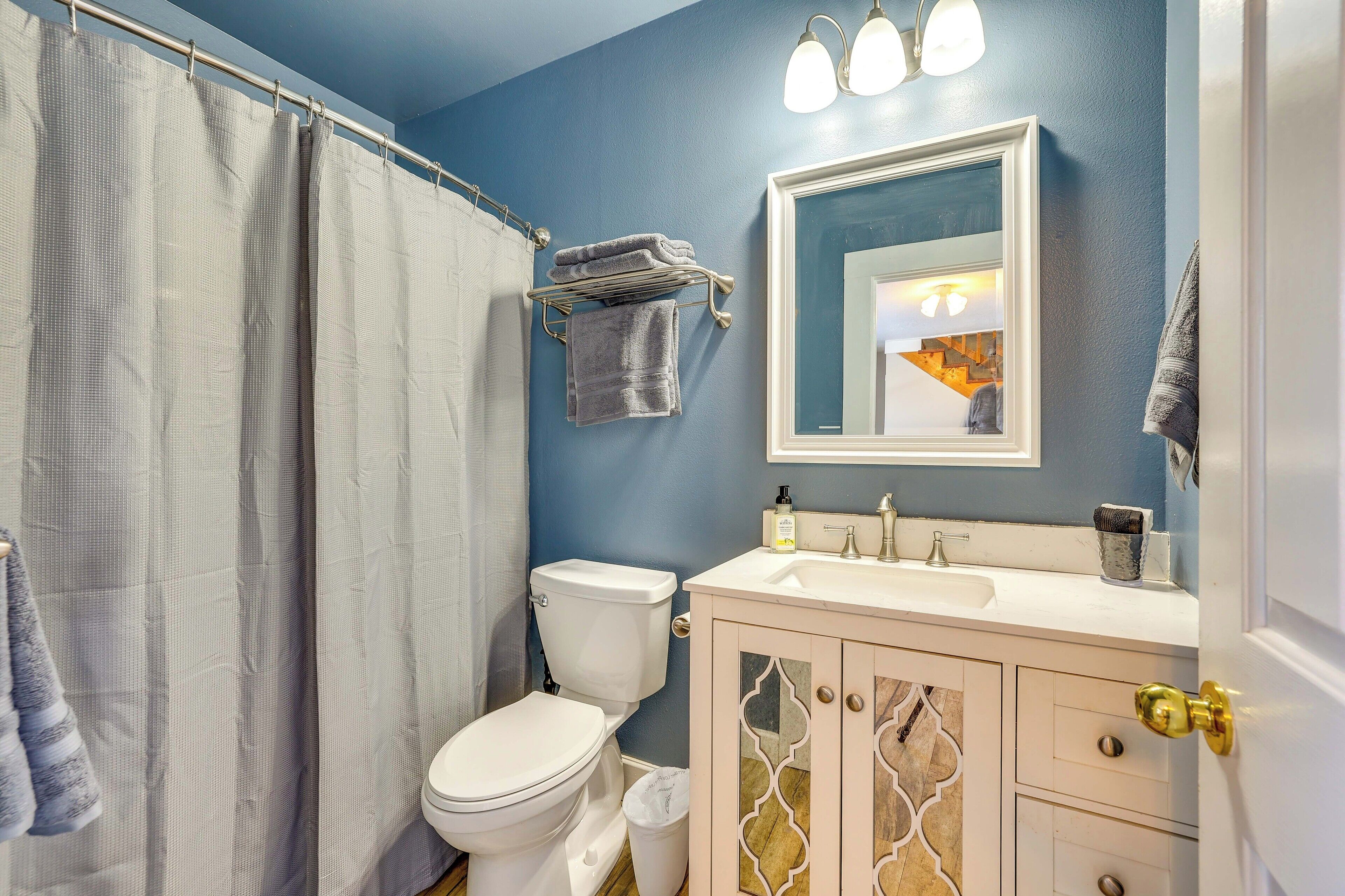 Une salle de bain avec des toilettes blanches, un rideau de douche, un porte-serviettes avec des serviettes, un lavabo avec un miroir et un meuble avec des tiroirs.