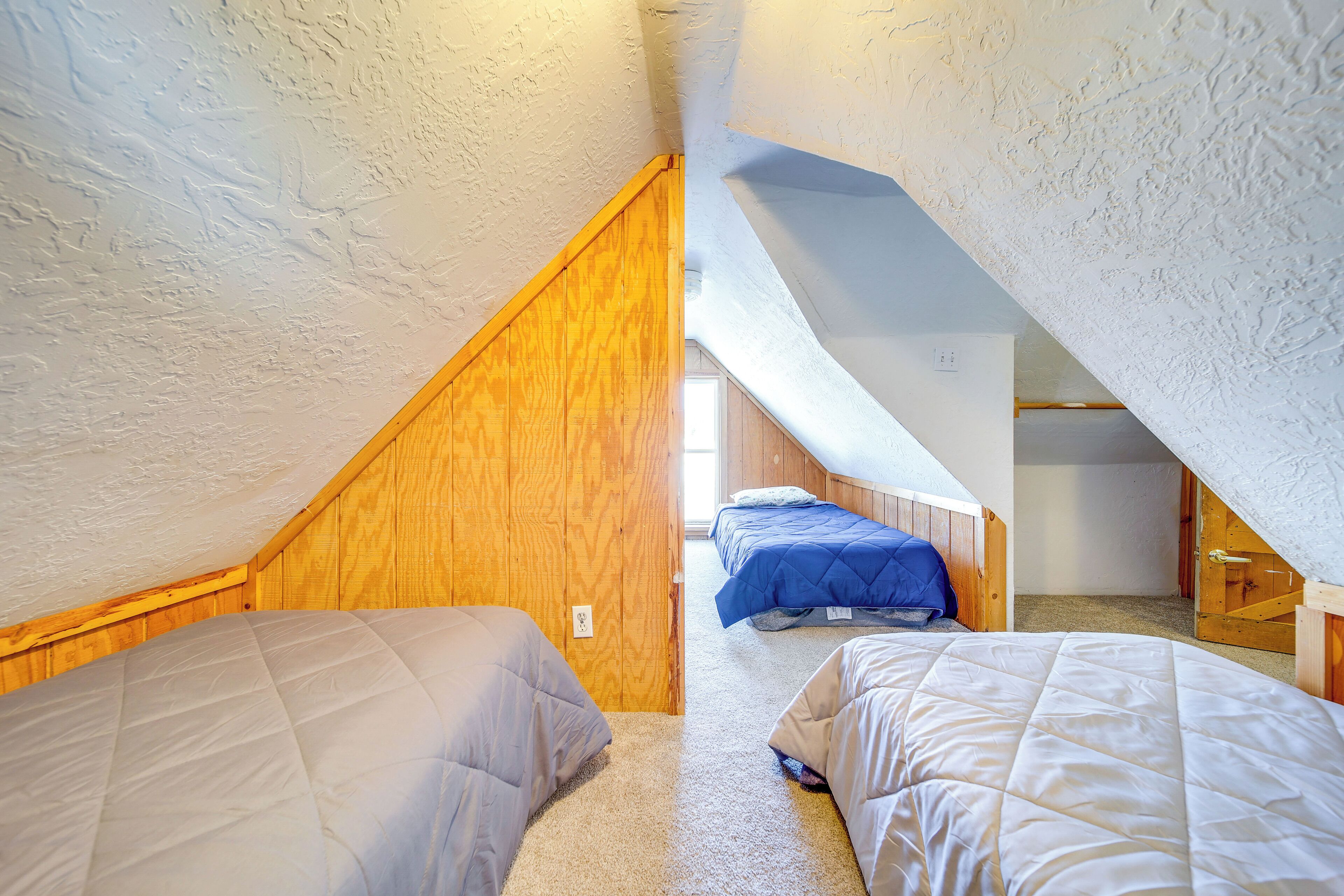 Un pequeño dormitorio en ático con dos camas, paredes de madera y techo inclinado.