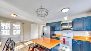 Una cucina con mobili blu, un'isola in legno con sgabelli, un lampadario e un fornello bianco.