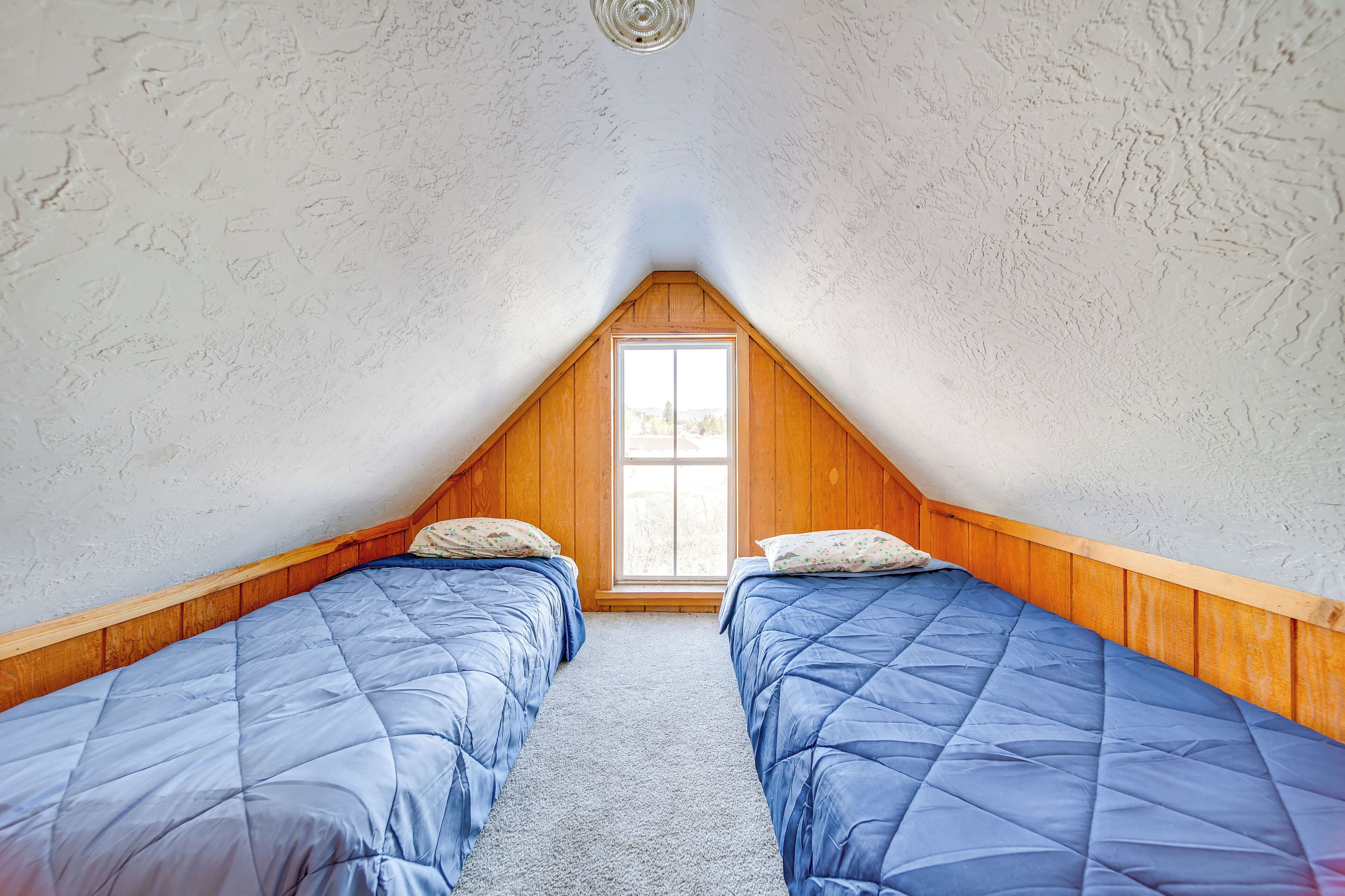 A small attic bedroom with two single beds, wooden walls, and a sloped ceiling.