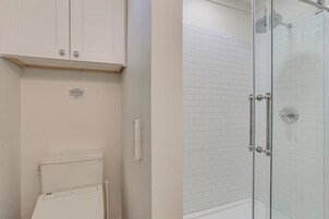 A bathroom with a toilet, a cabinet, and a glass-enclosed shower area.