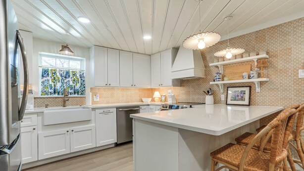 A modern kitchen with white cabinetry, a large island, wicker chairs, and a decorative backsplash. - Walk to Lake Texoma: Kingston Retreat w/ Deck! (Kingston)