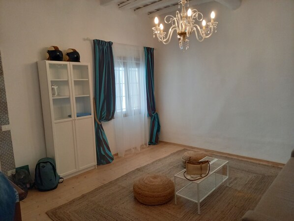 Une pièce avec un meuble blanc, un lustre, un pouf rond et une petite table sur laquelle se trouve un sac à main.