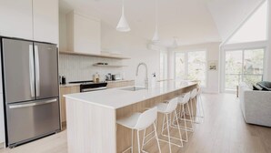 Una cocina moderna con un refrigerador de acero inoxidable, taburetes de bar blancos y una isla grande.