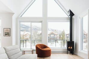 A modern living room with a large window, a fireplace, and a cozy chair.