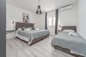 Ein Schlafzimmer mit zwei Betten, einer Hängelampe, einer Klimaanlage und einem Fenster mit Vorhängen.