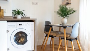 A compact kitchen with a built-in washing machine, a dining area with two chairs, and a potted plant on the table. - Lovely & bright Brighton beach retreat by the sea (Brighton and Hove)