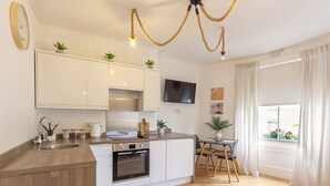 A modern kitchen with white cabinetry, a built-in oven, and a dining area with a table and chairs. - Lovely & bright Brighton beach retreat by the sea (Brighton and Hove)