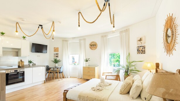 A modern bedroom with a wooden bed, a kitchen area, and a dining space. - Lovely & bright Brighton beach retreat by the sea (Brighton and Hove)