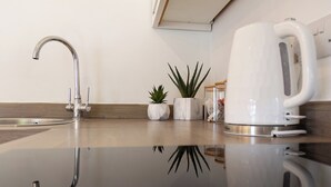 A modern kitchen with a stainless steel faucet, a white kettle, and two potted plants on the countertop. - Lovely & bright Brighton beach retreat by the sea (Brighton and Hove)