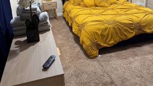 Een hotelkamer met een bed, nachtkastje, lamp, afstandsbediening en een sierplant.