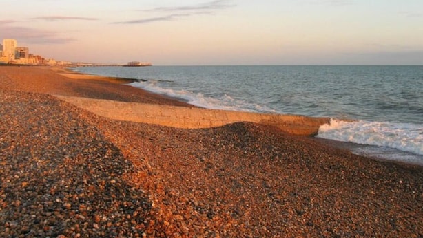 A pebbled beach with a calm sea and a clear sky.