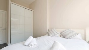 A hotel room with a bed, two patterned pillows, and a rolled towel on the bed.