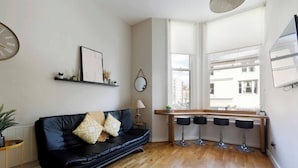 A modern living room with a black leather sofa, a wooden coffee table, and a dining area with three black bar stools.