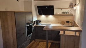 A compact kitchen with wooden cabinets, a built-in oven, a sink, and a flat-screen TV mounted above the countertop.