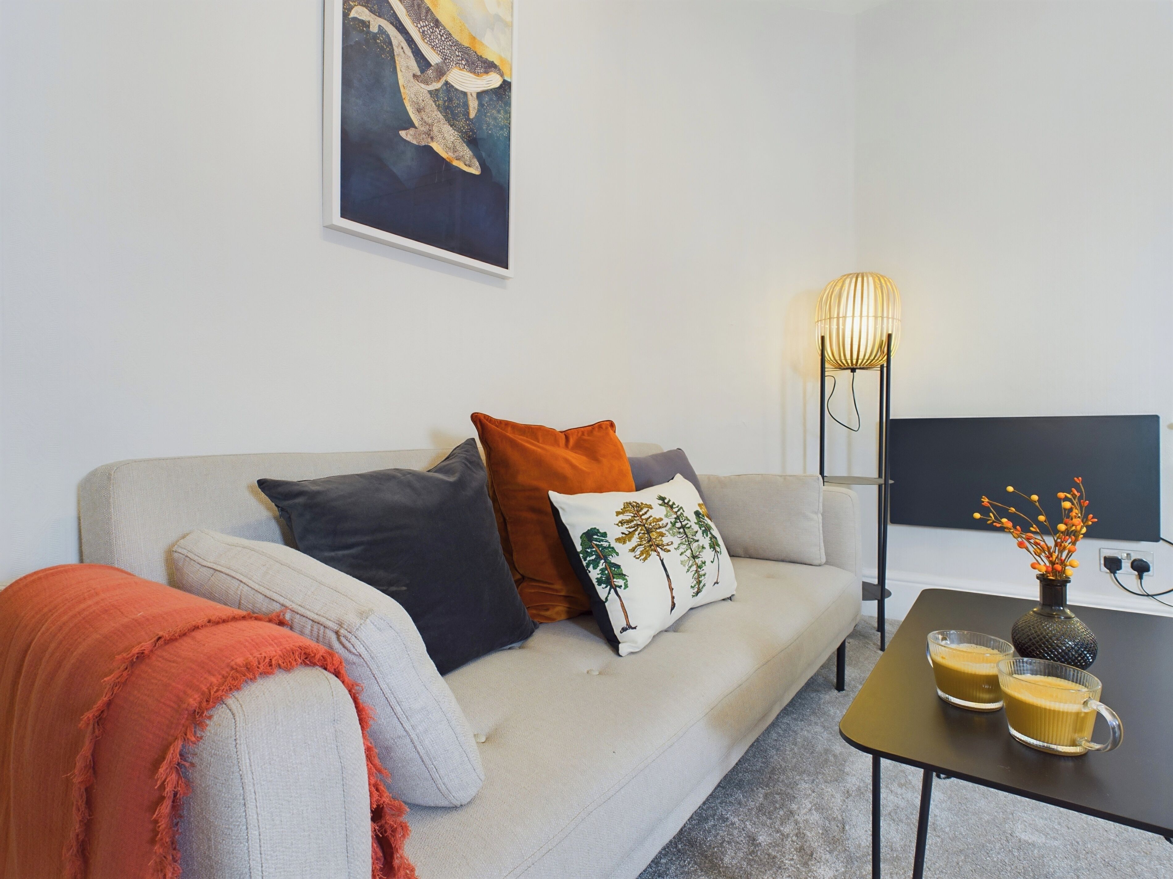 Uma sala de estar moderna com um sofá, almofadas, uma mesa de centro, um abajur e um quadro na parede.