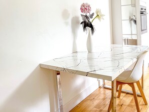 A white marble dining table with a white chair, a vase with flowers, and a kitchen in the background. - London 2-bed Apartment in Herbert Road (London)