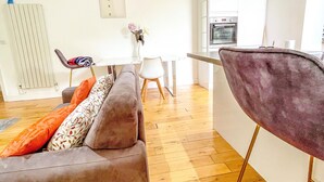 A modern living room with a sofa, a dining table, and a kitchen area with an oven. - London 2-bed Apartment in Herbert Road (London)