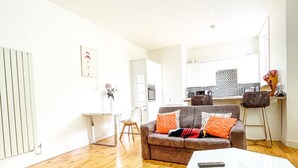 A modern living room with a sofa, a coffee table, and a dining area with a kitchen in the background. - London 2-bed Apartment in Herbert Road (London)