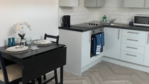 Una cocina compacta con armarios blancos, encimera negra y suelo de madera en espiga.