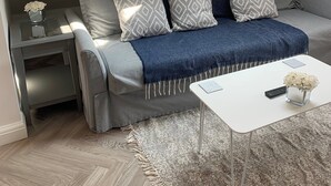 Un dormitorio tipo loft acogedor con tragaluces, un sofá gris con cojines estampados, una mesa de centro blanca y un jarrón decorativo.