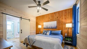 Una camera da letto con un letto, due abat-jour, una ventola a soffitto, un quadro e una finestra con tende.