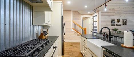 Una cocina moderna con estufa a gas, armarios blancos y piso de madera.
