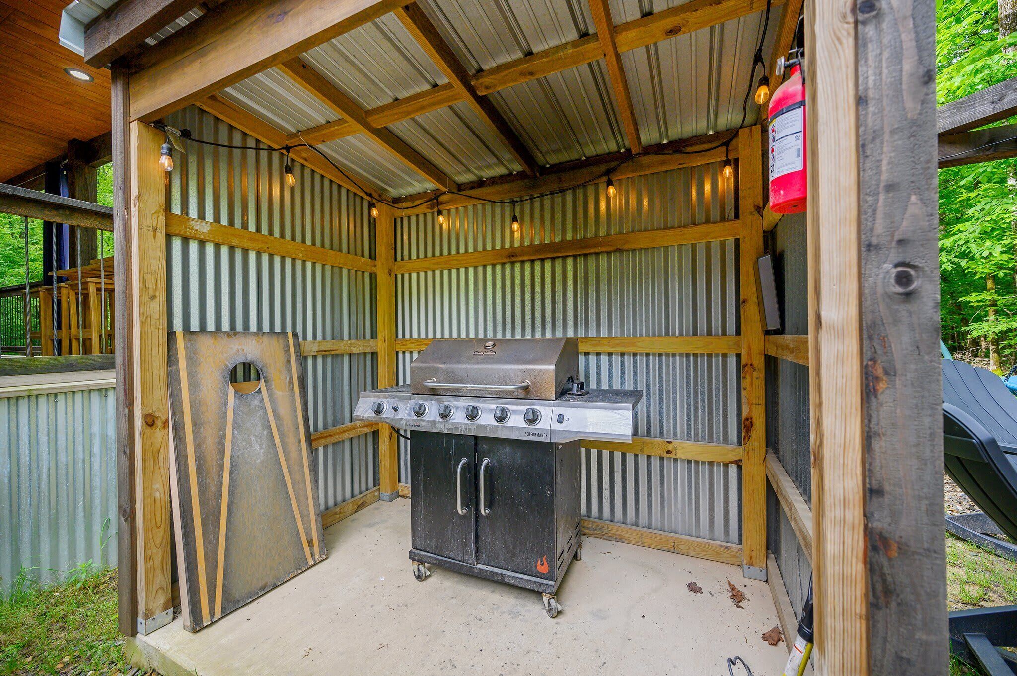 Ein Grillplatz mit Metallgrill, Schornstein, Feuerlöscher und einer Holzhütte mit Wellblechdach.