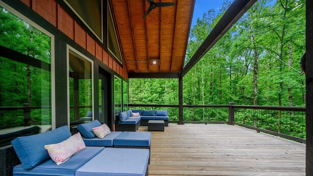 Una terrazza coperta con posti a sedere all'aperto e ampie finestre che si affacciano su una foresta.