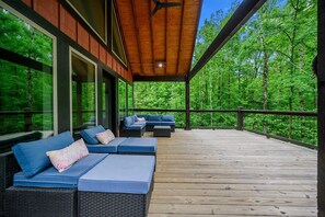 Eine überdachte Terrasse mit Sitzgelegenheiten und großen Fenstern mit Blick auf einen Wald.