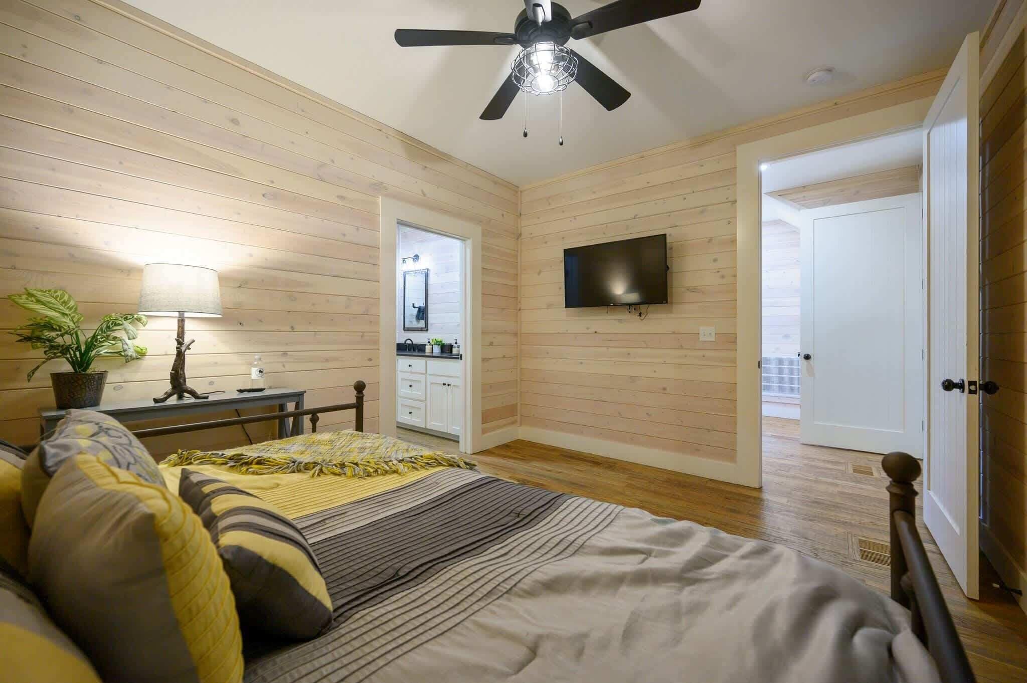 Een slaapkamer met een bed, een plafondventilator, een televisie en een deur naar een badkamer.