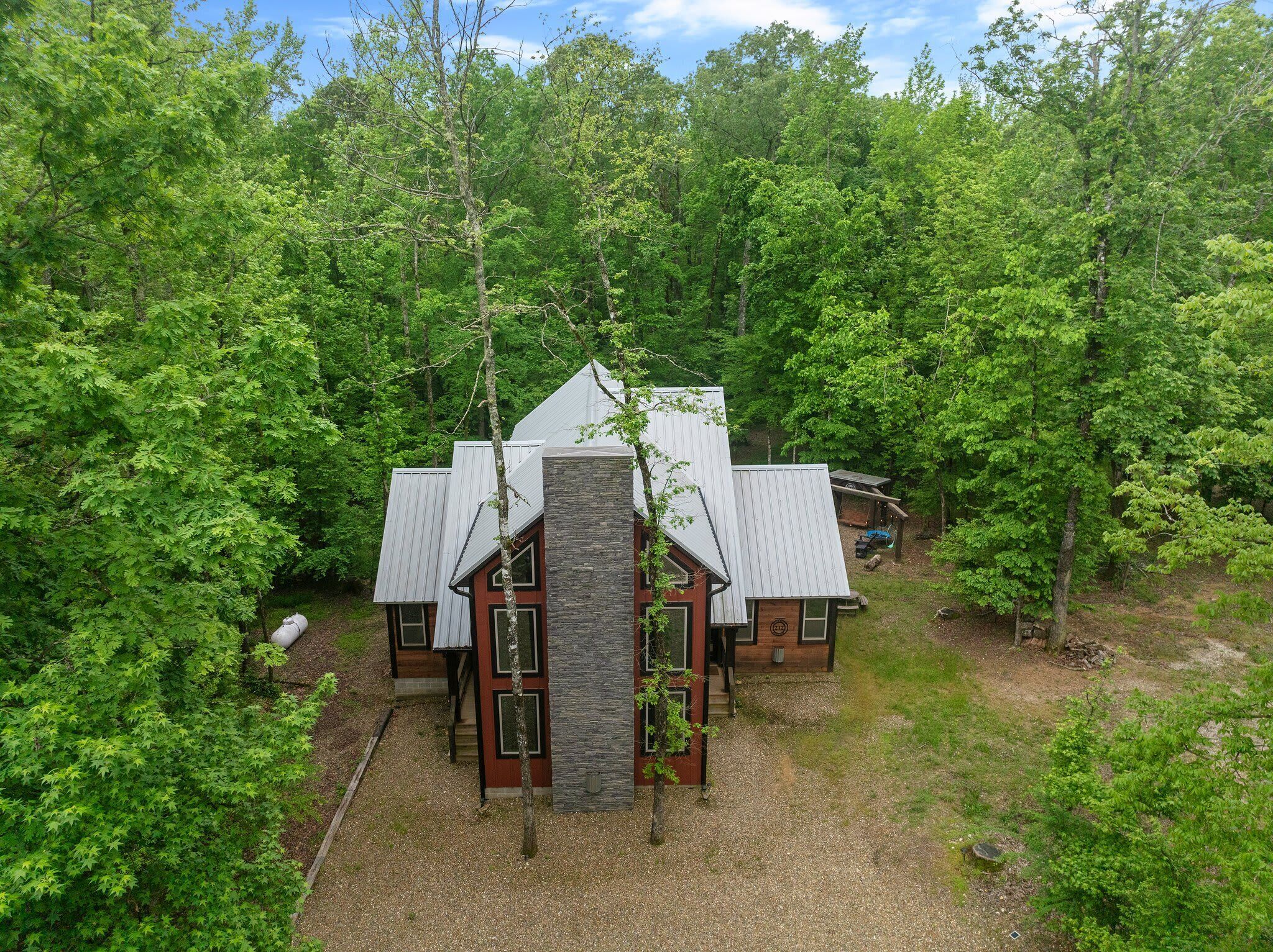Une cabane dotée d’une cheminée en pierre centrale, entourée d’une forêt dense.