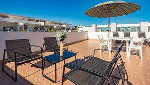 Terraza en la azotea con mobiliario exterior, que incluye sillas y una mesa, además de un amplio paraguas.