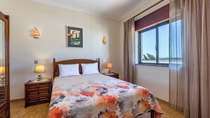 Habitación de hotel con una cama grande, dos mesitas de noche con lámparas, un cuadro en la pared y una ventana con cortinas.