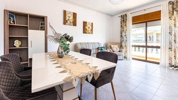 Una sala de estar moderna con una mesa de comedor, sillas, un sofá y un balcón con cortinas.