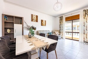 Una sala de estar moderna con una mesa de comedor, sillas, un sofá y un balcón con cortinas.