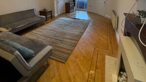 A spacious living room with a large sofa, a fireplace, and a view of the outside through a large window. - Westgate Haven - Spacious 4 Bedroom Apartment (Newcastle-upon-Tyne)
