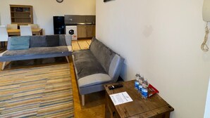 A modern living room with a sofa, a wooden coffee table, and a kitchen area in the background. - Westgate Haven - Spacious 4 Bedroom Apartment (Newcastle-upon-Tyne)