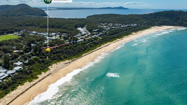 Ein Luftbild einer Küstenregion mit Strand, Häusern und einem bewaldeten Hügel.