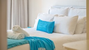 Ein ordentlich bezogenes Bett mit weißer und blauer Bettwäsche, ein aufgerolltes weißes Handtuch und eine blaue Decke.