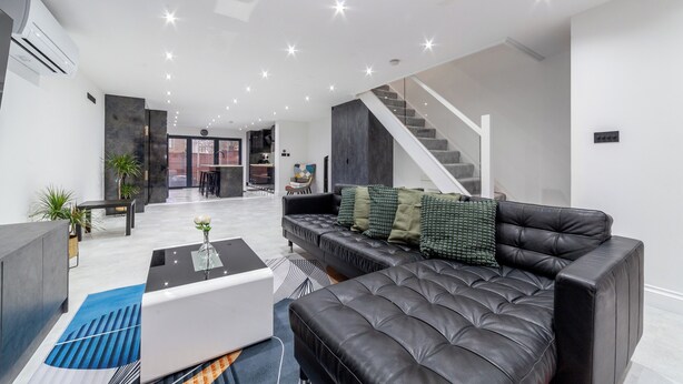 Una sala de estar moderna con un sofá de cuero negro, una mesa de centro de vidrio y una escalera que lleva a otro nivel.