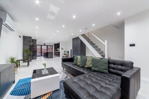 A modern living room with a black leather sofa, a glass coffee table, and a staircase leading to another level. - Stonewall Superb Cozy House (London)