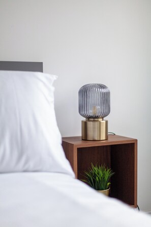 A bed with white bedding, a bedside table with a lamp, and a small plant. - Stonewall Superb Cozy House (London)