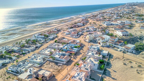 An aerial view of a coastal town with white buildings, sandy streets, and a beach in the background.